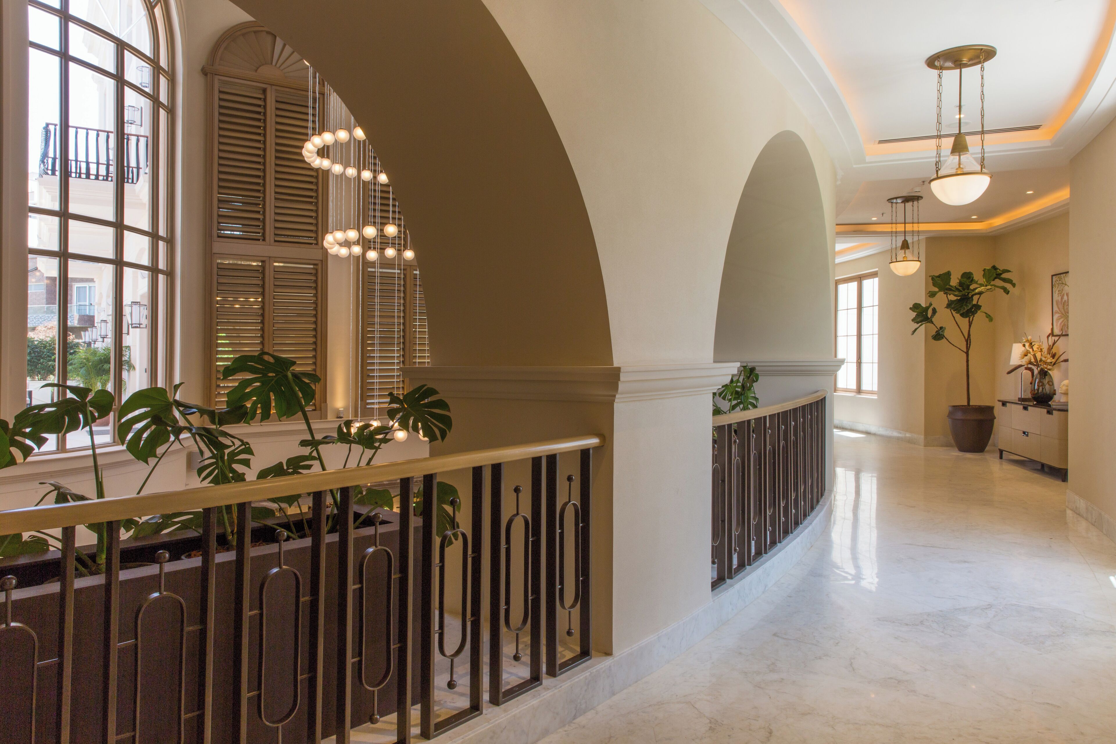 A spacious hallway with arched ceilings, large windows, and potted plants.