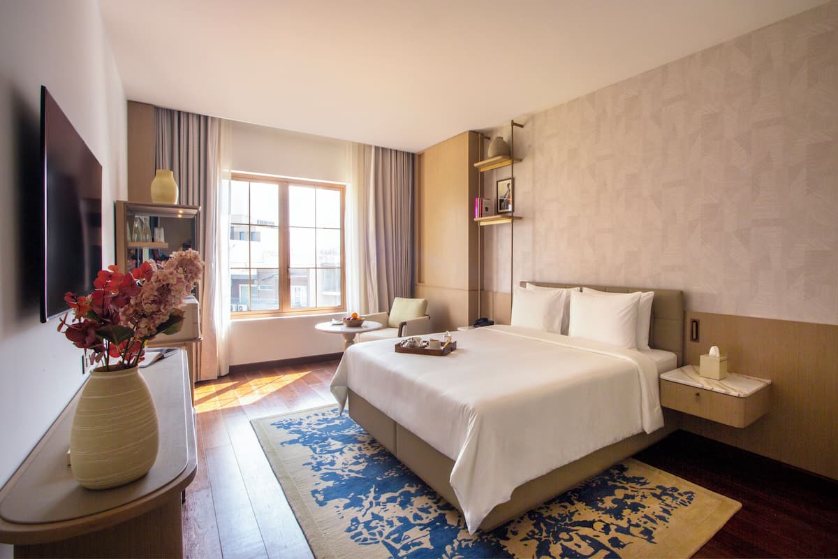 Habitación de hotel con cama, mesita de noche y ventana con cortinas.
