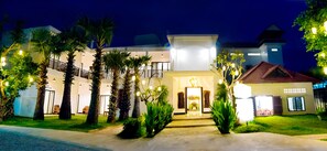 A well-lit hotel entrance with a central doorway, palm trees, and a pathway leading to the entrance. - Borei Hang Tep Residence & Spa (Siem Reap)