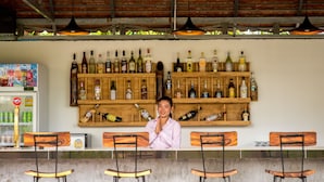 Un coin bar doté d’étagères en bois où sont rangées différentes bouteilles d’alcool, d’un réfrigérateur rempli de boissons et de quatre tabourets de bar en bois.