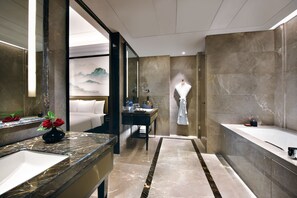 Une salle de bain moderne avec un grand miroir, un meuble-lavabo doté d’un plan en marbre, une baignoire et un peignoir accroché au mur.