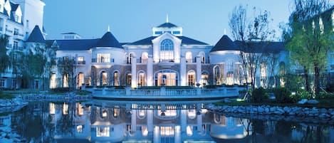 A large, multi-story building with a symmetrical facade, a central dome, and a reflective water feature in front.