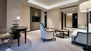 Une chambre d’hôtel moderne avec une table ronde, deux chaises, un canapé, un bureau avec une lampe et un téléviseur à écran plat.