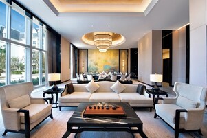 A modern hotel lobby with a seating area, a dining setup, and a large window offering a view of the outside.