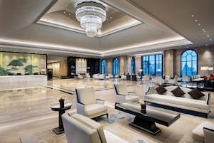 A spacious lobby with a high ceiling, elegant chandeliers, and a reception desk.