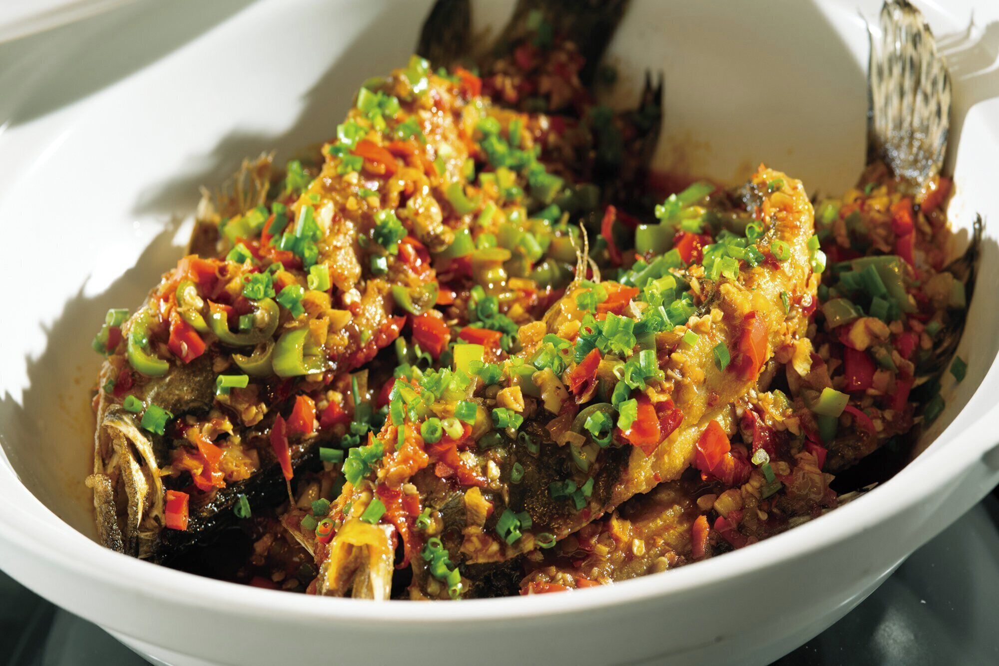 A bowl of cooked fish with vegetables and green onions.