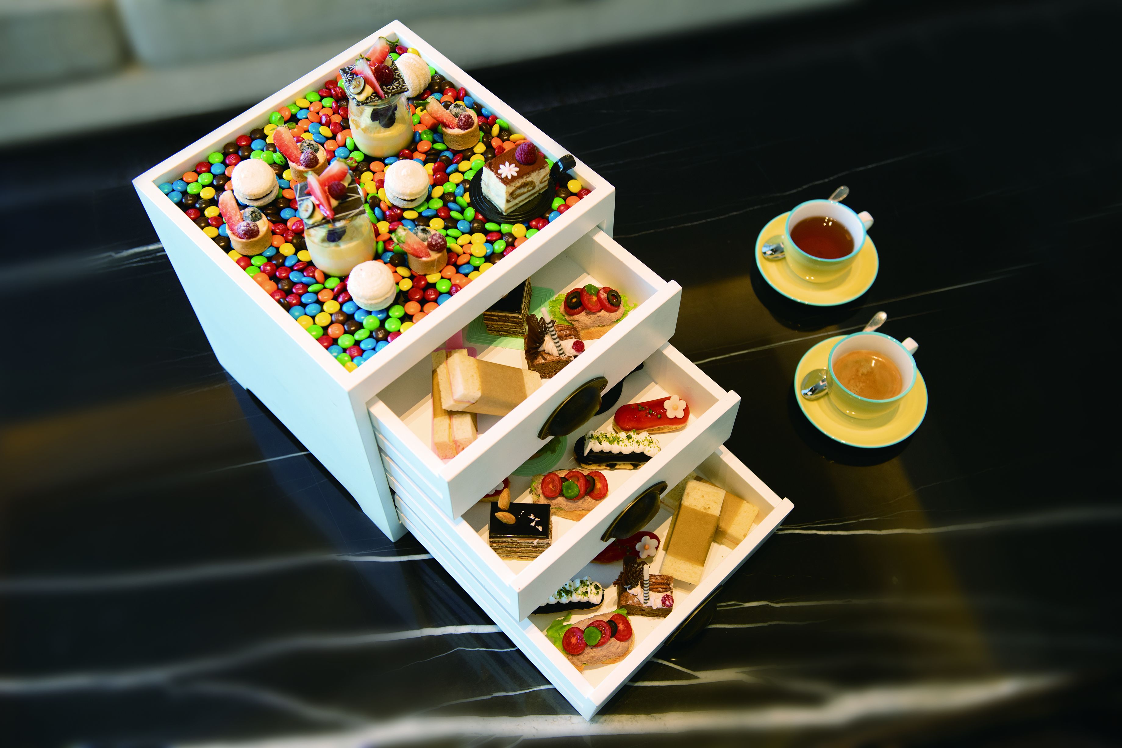 Eine Dessertauslage mit mehreren Tabletts voller verschiedener Süßigkeiten und zwei Tassen Tee.