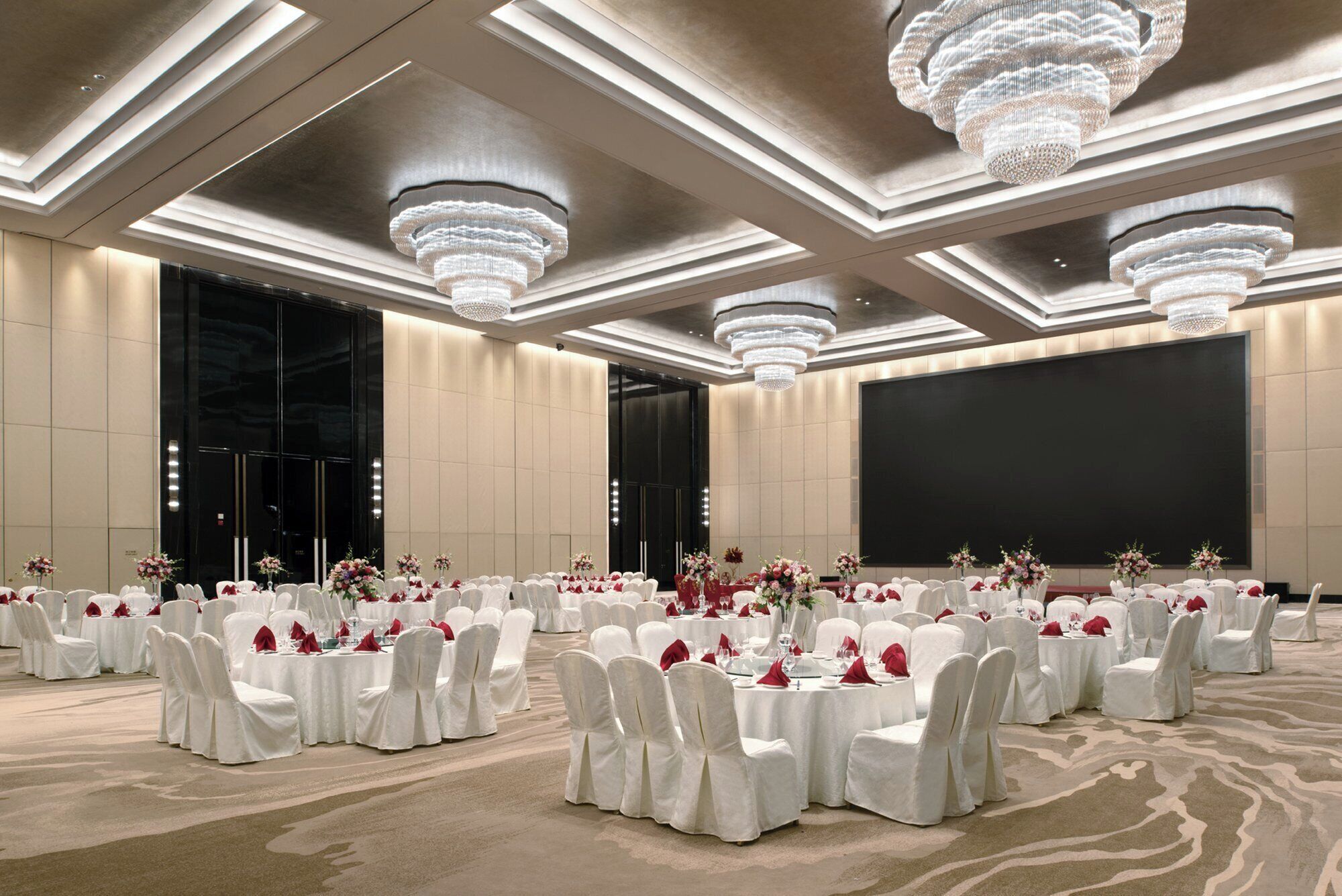 Une salle de banquet avec des tables rondes, des chaises blanches et des lustres.