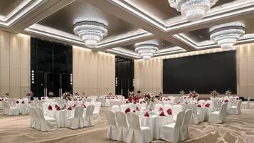 Une salle de banquet avec des tables rondes, des chaises blanches et des lustres.