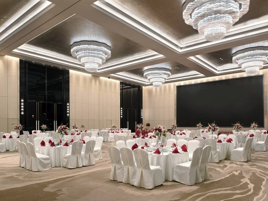 Une salle de banquet avec des tables rondes, des chaises blanches et des lustres.