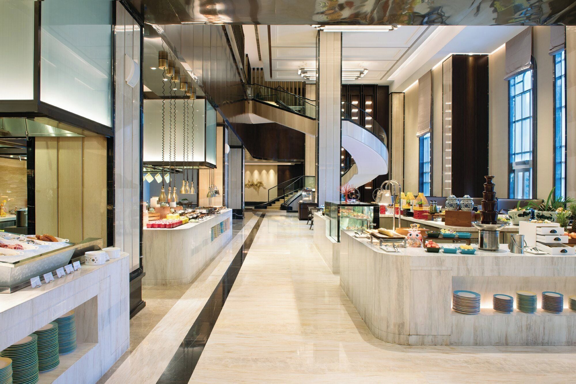 A modern hotel lobby with a central bar area, a staircase, and a view of the cityscape through large windows.