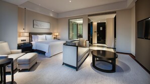 Una habitación de hotel moderna con cama, sofá, mesa de centro, televisión y un espejo grande.