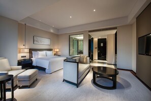 Una habitación de hotel moderna con cama, sofá, mesa de centro, televisión y un espejo grande.