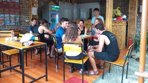 A rustic dining area with wooden tables and chairs, a brick wall, and a bamboo ceiling. - Tam Coc Riverside homestay (Nam Hoa Lu)