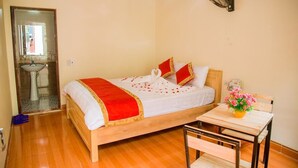 A neatly arranged bedroom with a wooden bed, a bedside table with a vase of flowers, and a small table with a chair. - Tam Coc Riverside homestay (Nam Hoa Lu)