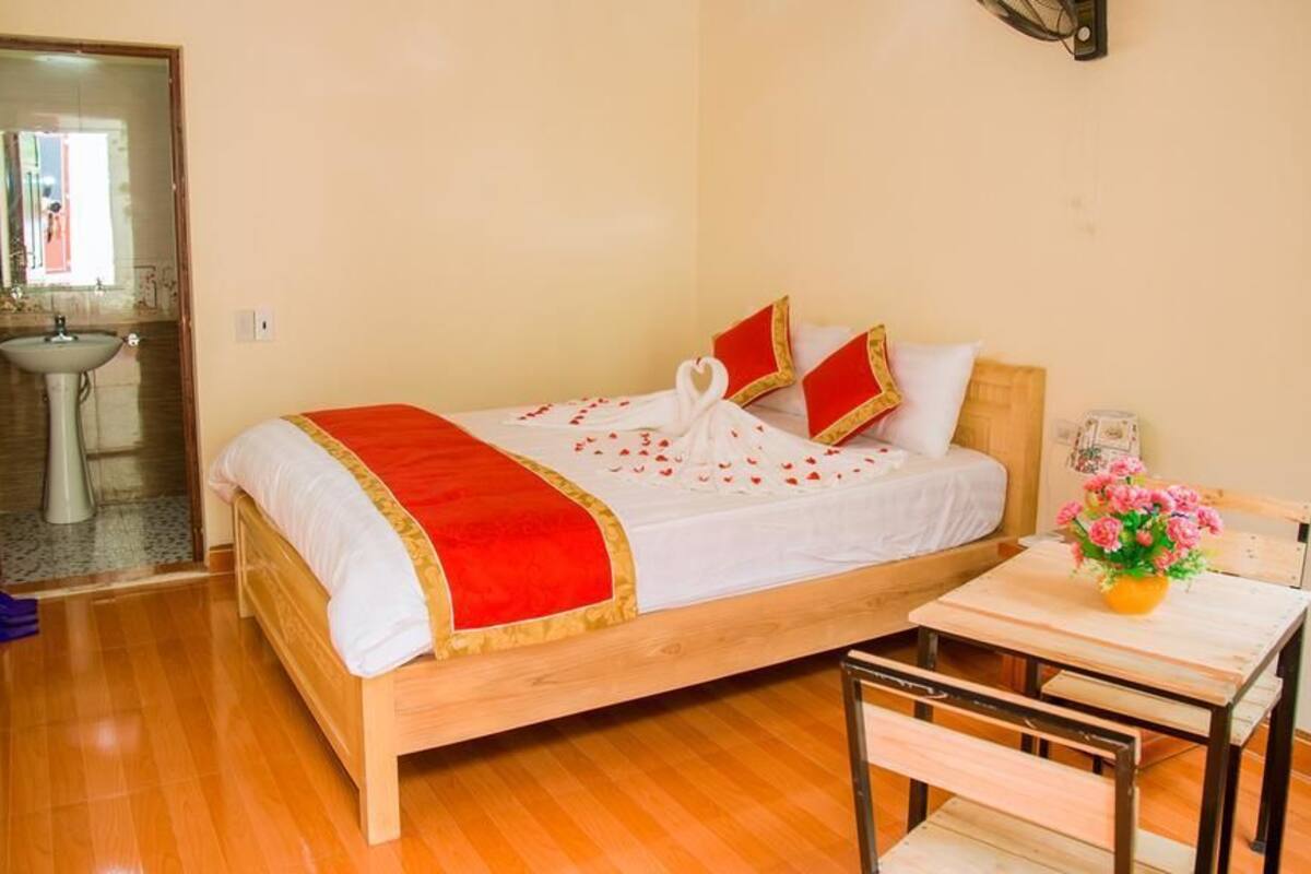 Une chambre à coucher bien rangée, avec un lit en bois, une table de chevet ornée d’un vase de fleurs et une petite table accompagnée d’une chaise.