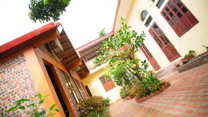 A courtyard with a brick floor, a tree with green fruit, and a building with red doors and windows. - Tam Coc Riverside homestay (Nam Hoa Lu)