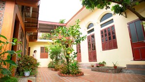 A courtyard with a tiled floor, potted plants, and a building with red doors and windows. - Tam Coc Riverside homestay (Nam Hoa Lu)