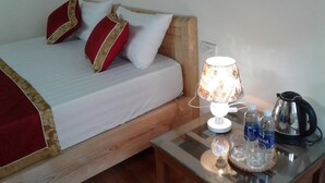A bed with a wooden headboard, two red pillows with gold trim, a white pillow, a table with a lamp, water bottles, a glass, and a kettle. - Tam Coc Riverside homestay (Nam Hoa Lu)