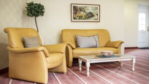 Een kamer met twee gele leren fauteuils, een glazen bijzettafel met een schaal, een schilderij aan de muur en een plant in pot.