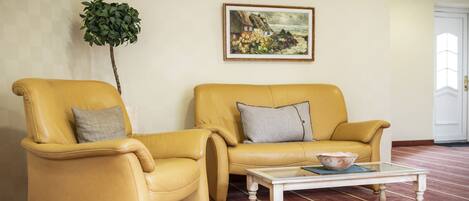 A room with two yellow leather armchairs, a glass coffee table with a bowl, a painting on the wall, and a potted plant.