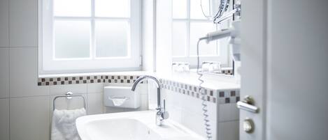 A modern bathroom with a white sink, a mirror, and a window.