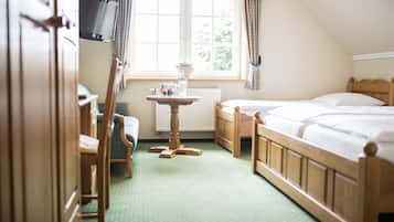 Habitación de hotel con cama de madera, una mesita con una planta, una silla y un televisor en la pared.