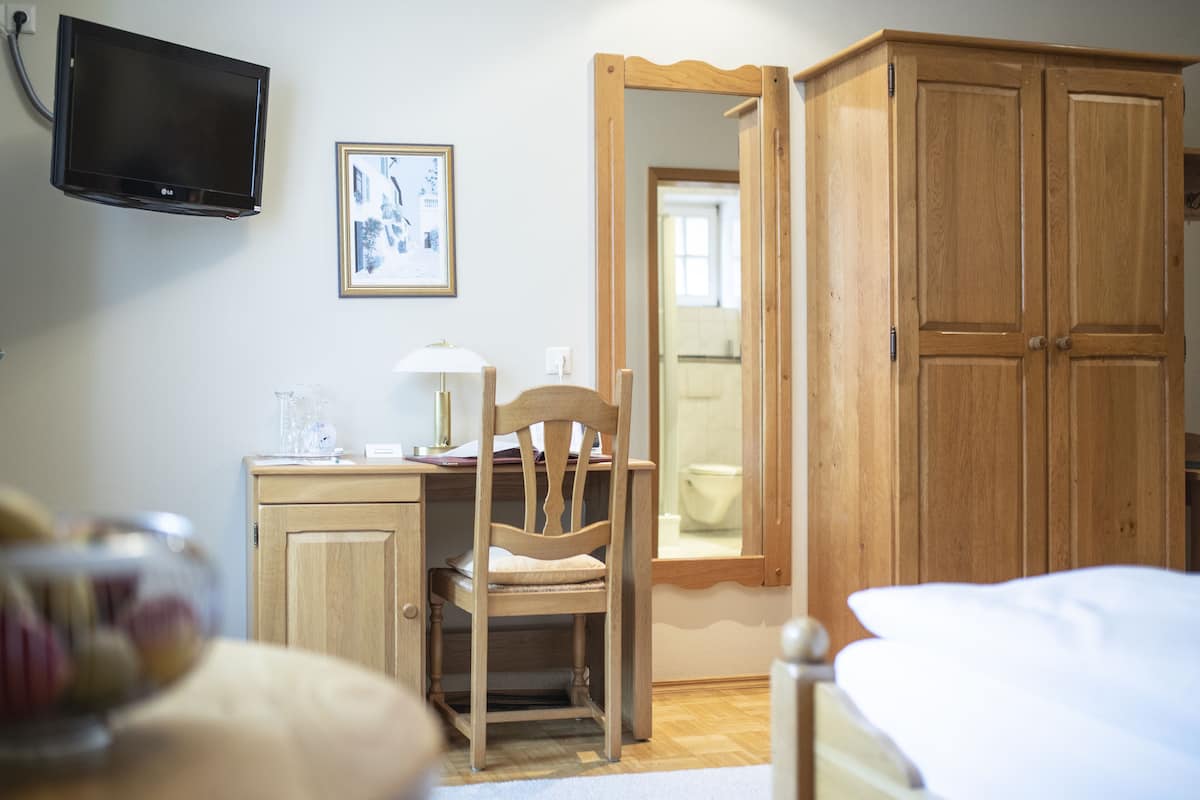 Une chambre à coucher comprenant un lit, une armoire en bois, un bureau avec une chaise, un téléviseur et un tableau encadré accroché au mur.