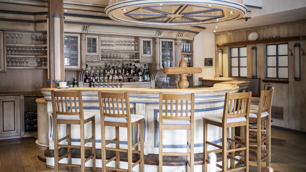 Een bar met een rond aanrecht, houten barstoelen en een grote, decoratieve plafondlamp.