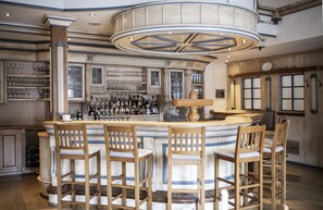Een bar met een rond aanrecht, houten barstoelen en een grote, decoratieve plafondlamp.