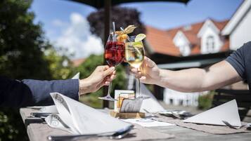 Dos personas brindando con copas de vino en una mesa al aire libre, con un menú y una botella de vino.