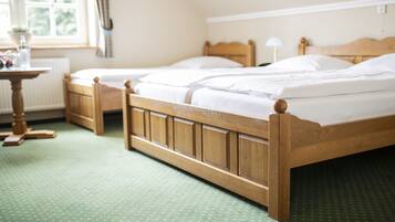 Habitación de hotel con dos camas de madera, una mesita y un ventanal con cortinas.