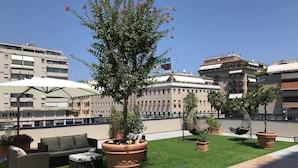 Una terraza en la azotea con mobiliario exterior, plantas en macetas y una vista despejada del paisaje urbano.