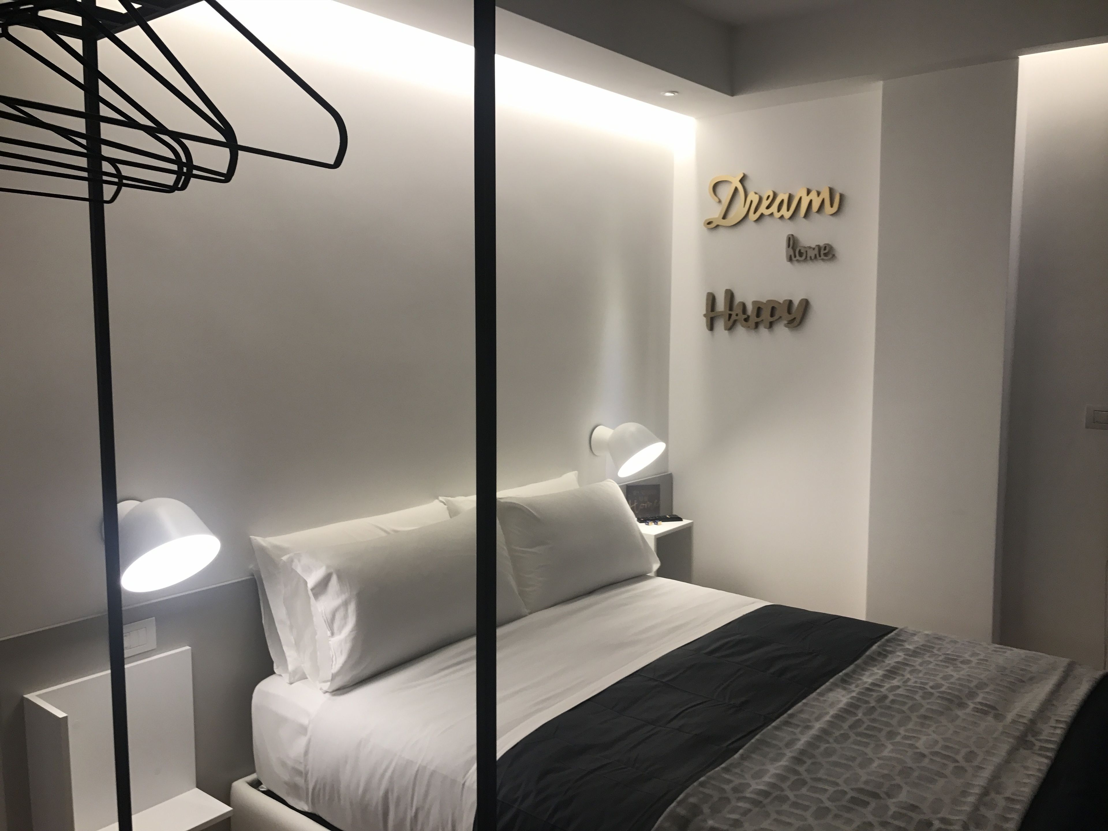 A neatly arranged bedroom with a bed, bedside lamps, a wall-mounted shelf, and decorative wall art.
