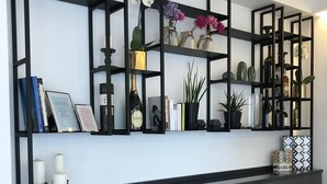 Un mueble de pared moderno con estructura negra y estantes que exhiben libros, objetos decorativos y plantas.