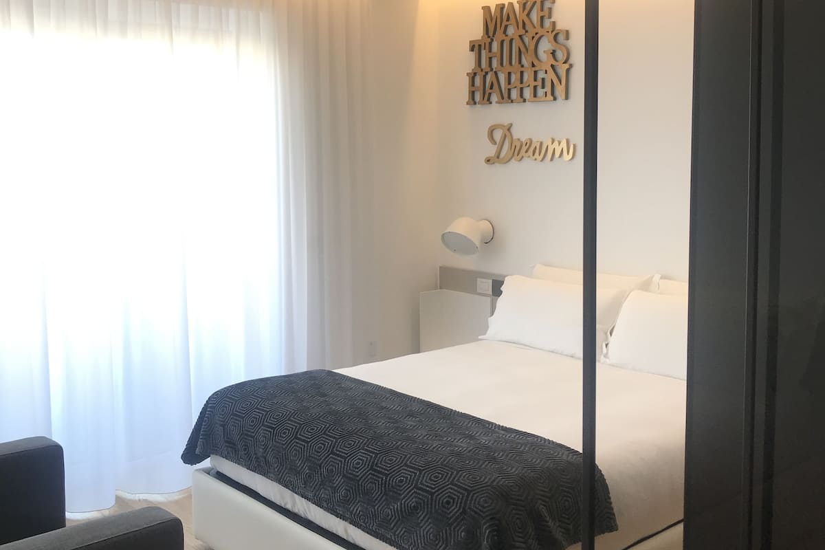 Una habitación de hotel moderna con una cama grande, una mesita de noche y una lámpara fijada en la pared.