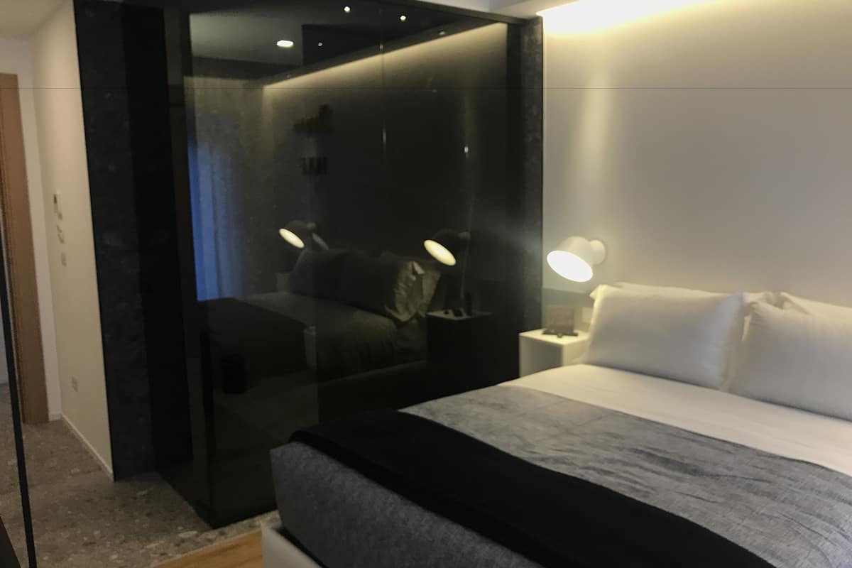 Un dormitorio moderno con una cama grande, una mesita de noche con lámpara y un armario de tonos oscuros.
