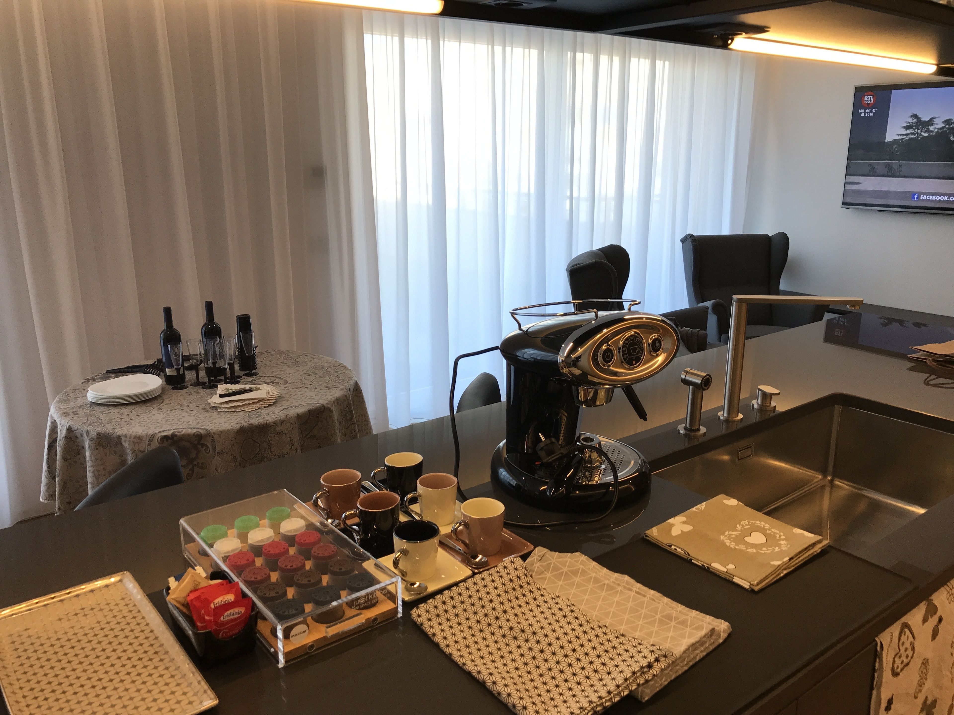 A modern kitchen with a coffee machine, a sink, and a dining area with a table set for two.