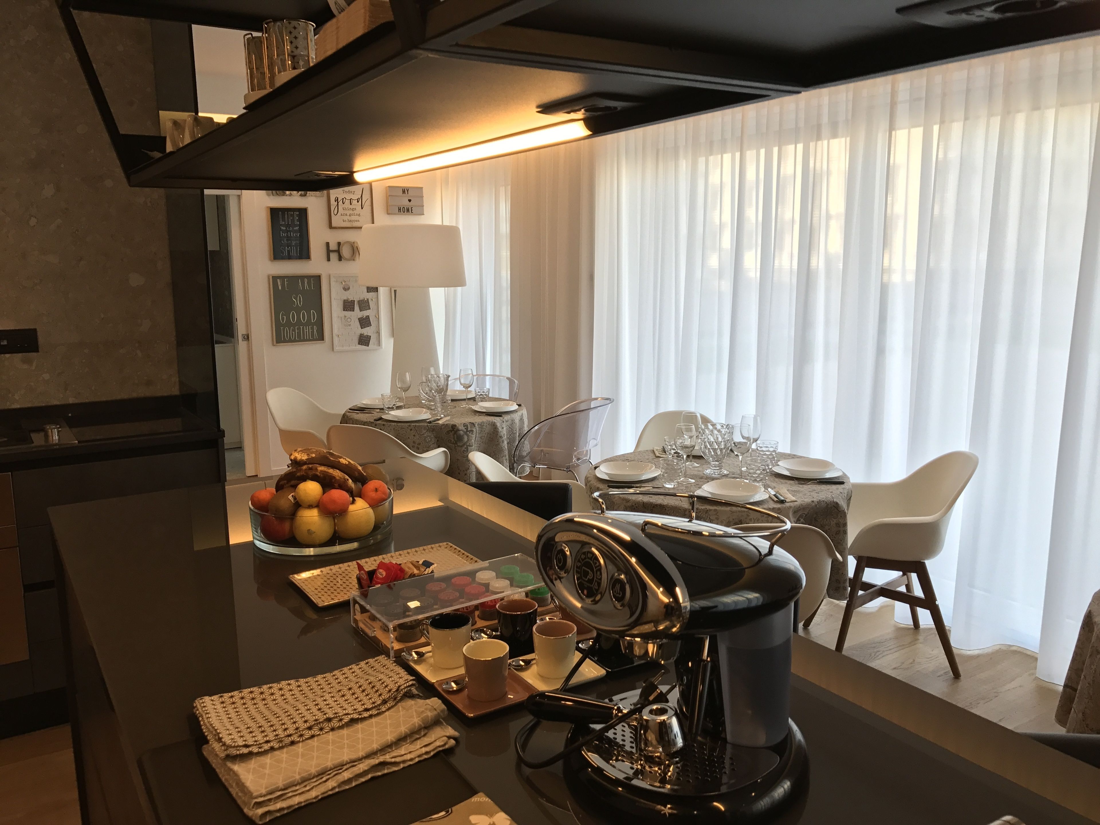 Cozinha moderna com máquina de café, fruteira e mesa de jantar posta para quatro pessoas.