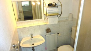 A small bathroom with a sink, toilet, and a mirror above the sink. There is a towel rack above the mirror and a shelf with toiletries. - Pension Münch - Am Anger (Nuenchritz)