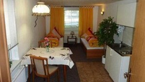 A compact room with a dining table, a sofa, a small table with a lamp, and a kitchenette. - Pension Münch - Am Anger (Nuenchritz)