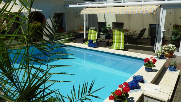 A swimming pool with a pergola and chairs, surrounded by potted plants and a palm tree. - Pension Münch - Am Anger (Nuenchritz)