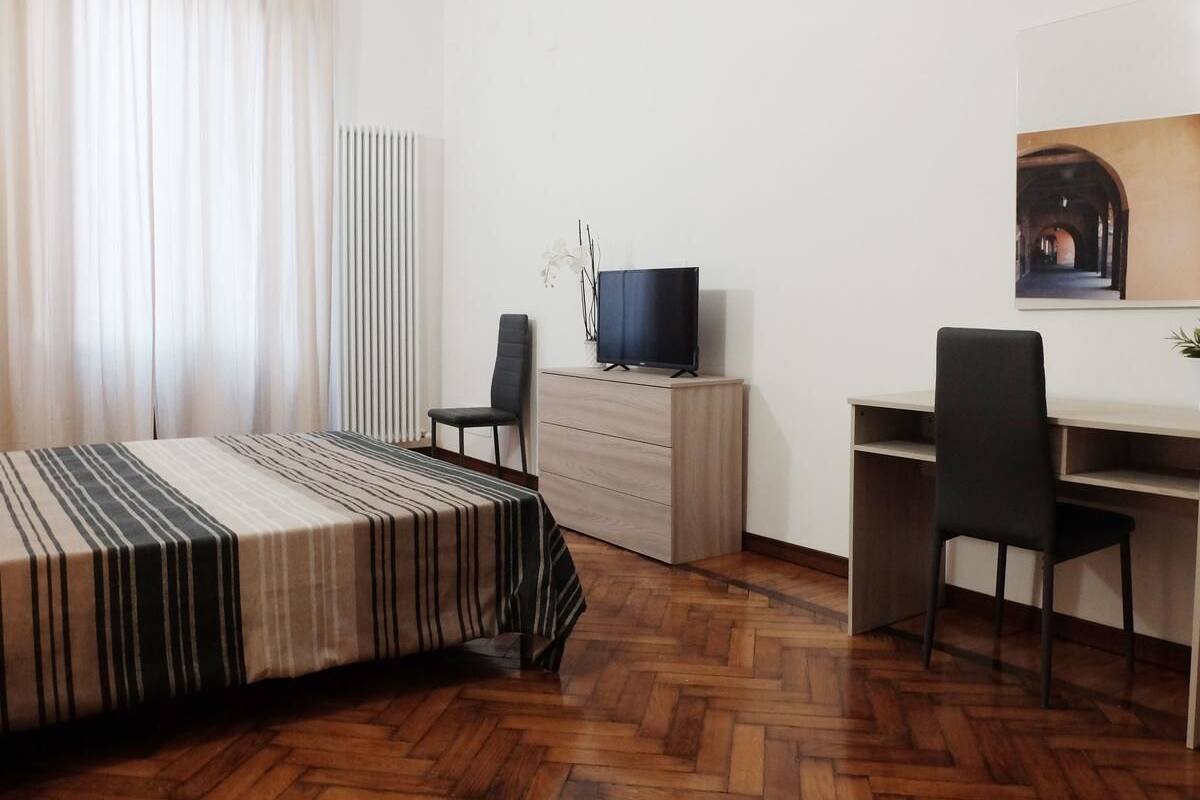 Un dormitorio con cama, escritorio, silla, televisor y cómoda.