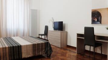 Una camera da letto con un letto, una scrivania, una sedia, una TV e un comò.