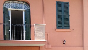 A building with a pink facade, a balcony with green shutters, and a stone wall. - Centro Storico Suites (Ferrara)