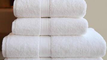 A stack of white towels arranged in a pyramid shape on a woven surface.