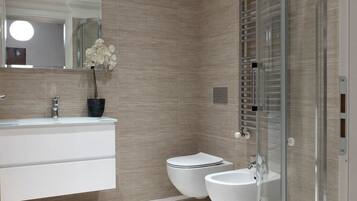 A modern bathroom with a glass shower enclosure, a white sink, and two toilets.