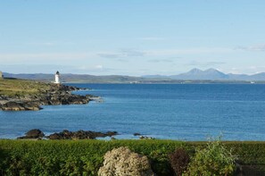 A coastal landscape with a lighthouse, rocky shoreline, and a view of distant mountains. - Port Charlotte Holidays (Islay Island)