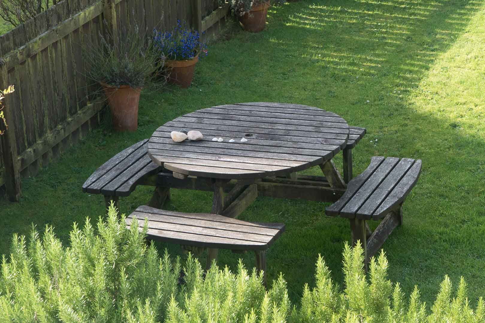 A wooden picnic table with benches, surrounded by grass and potted plants.