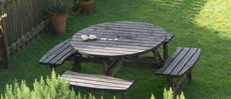 A wooden picnic table with benches, surrounded by grass and potted plants.